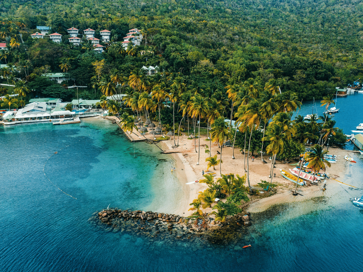 A scenic aerial view of a tropical island surrounded by lush greenery and turquoise waters under clear skies.