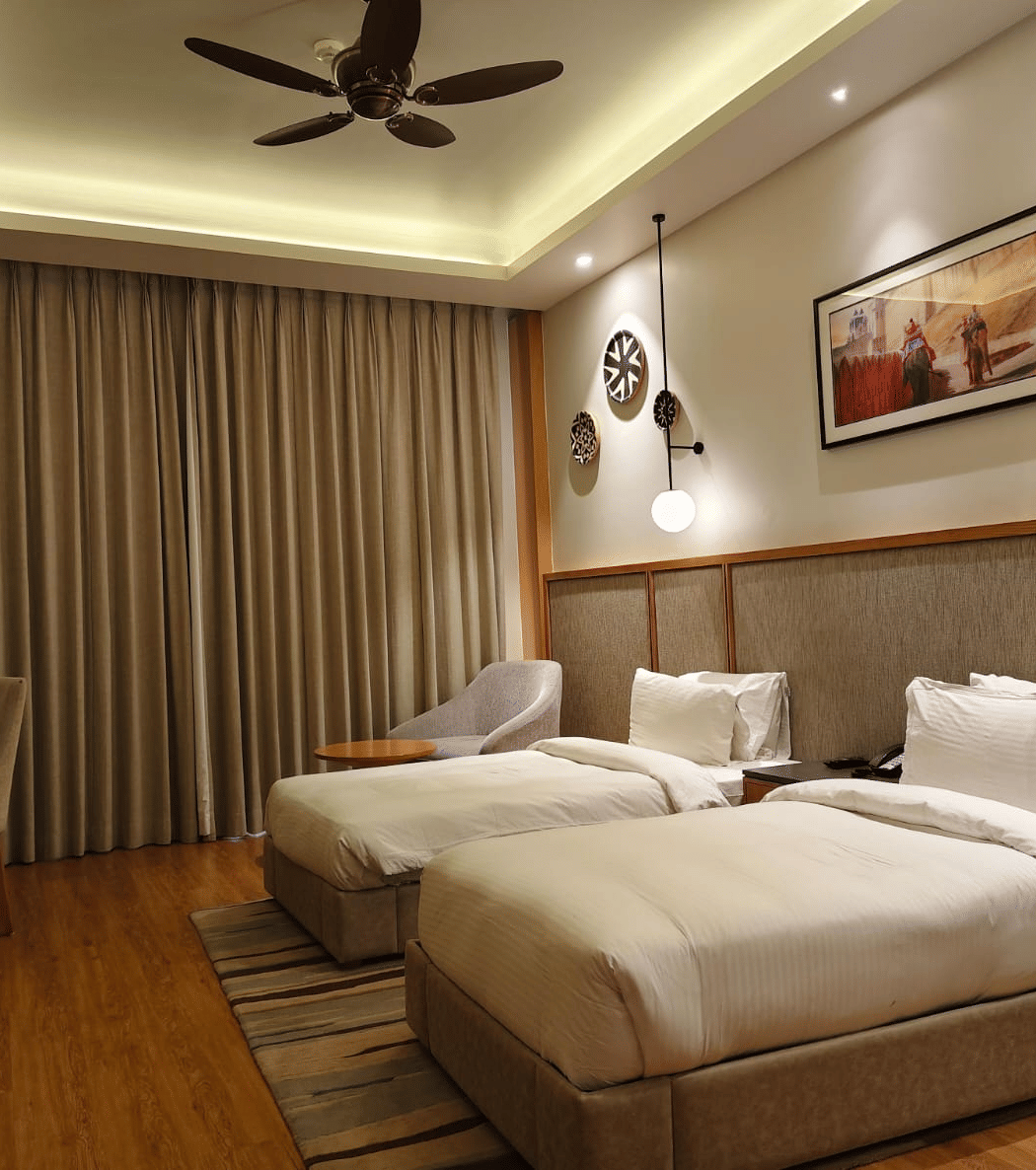 A modern hotel room or bedroom featuring two single beds, a wooden floor, a dark ceiling fan, recessed lighting, and a framed picture above the headboard.
