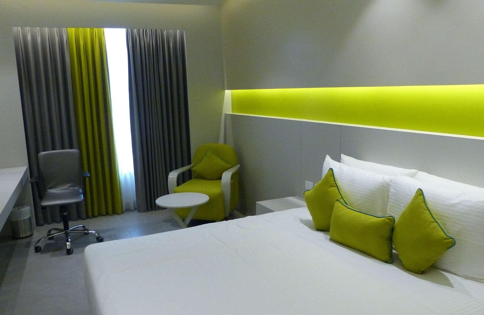  Spacious twin beds with headboards line the wall, large windows with curtains cover them, and a sofa is placed near the window