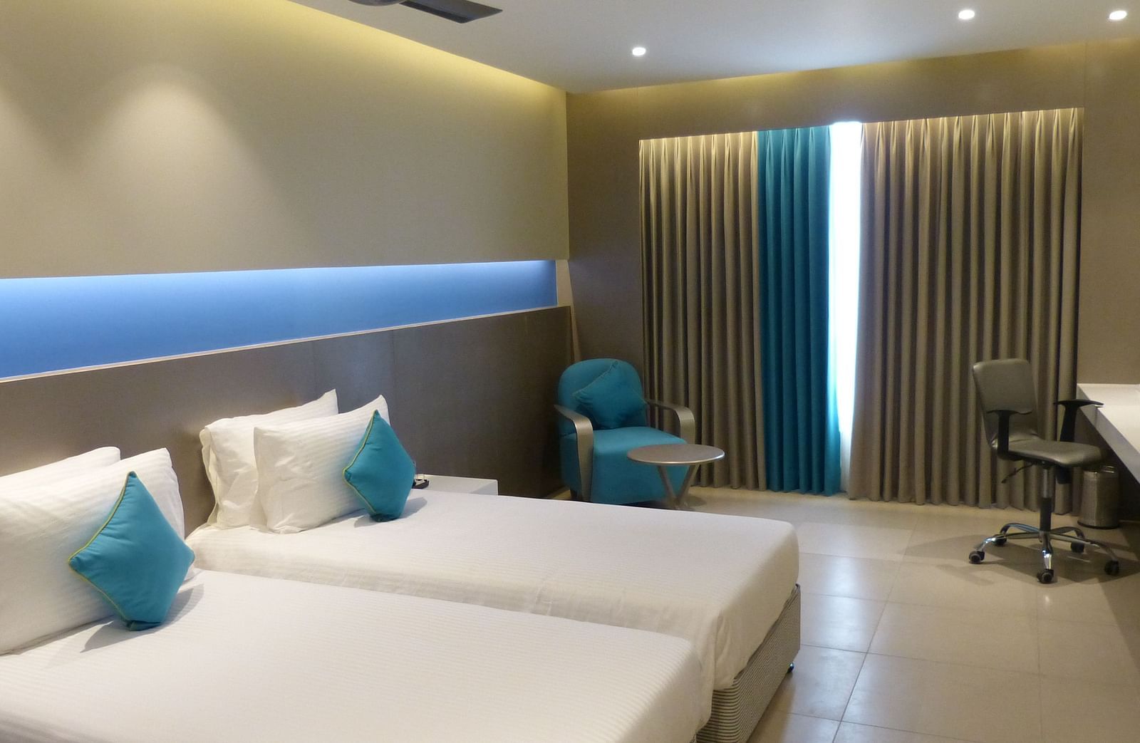  Spacious twin beds with headboards stretch across the wall, and large windows with curtains cover them