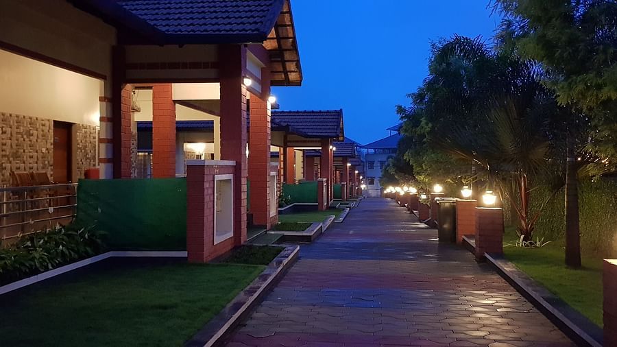 A nighttime view of a building is captured, illuminated by outdoor lighting, with a pathway leading towards it, set against a dark sky | Woodstock Resorts, Coorg