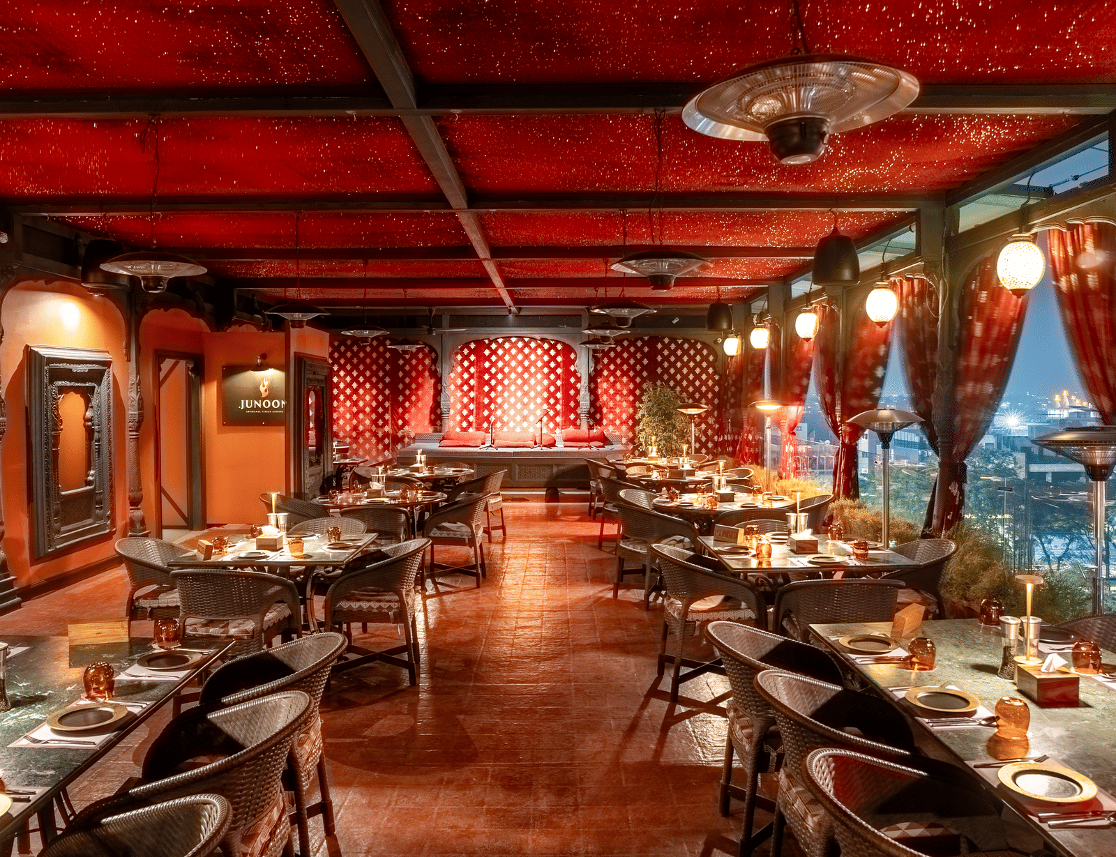 A large restaurant hall with red ceiling, long rows of dining tables and warm hanging lights at Infiniti Hotel, Indore.