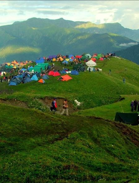 image of a hilly area with a lush green landscape and a serene views of the mountains in the background with people camping
