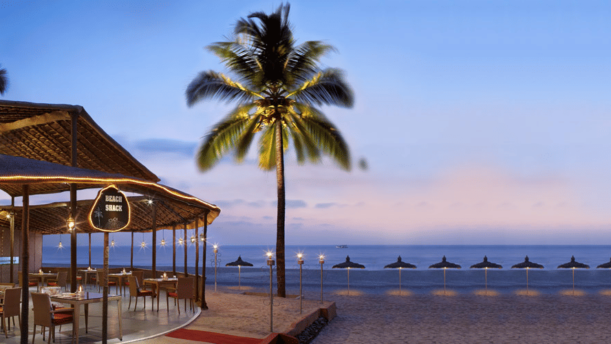 A beach shack with a coconut tree next to it at Caravela Beach Resort, Goa - restaurants in South Goa