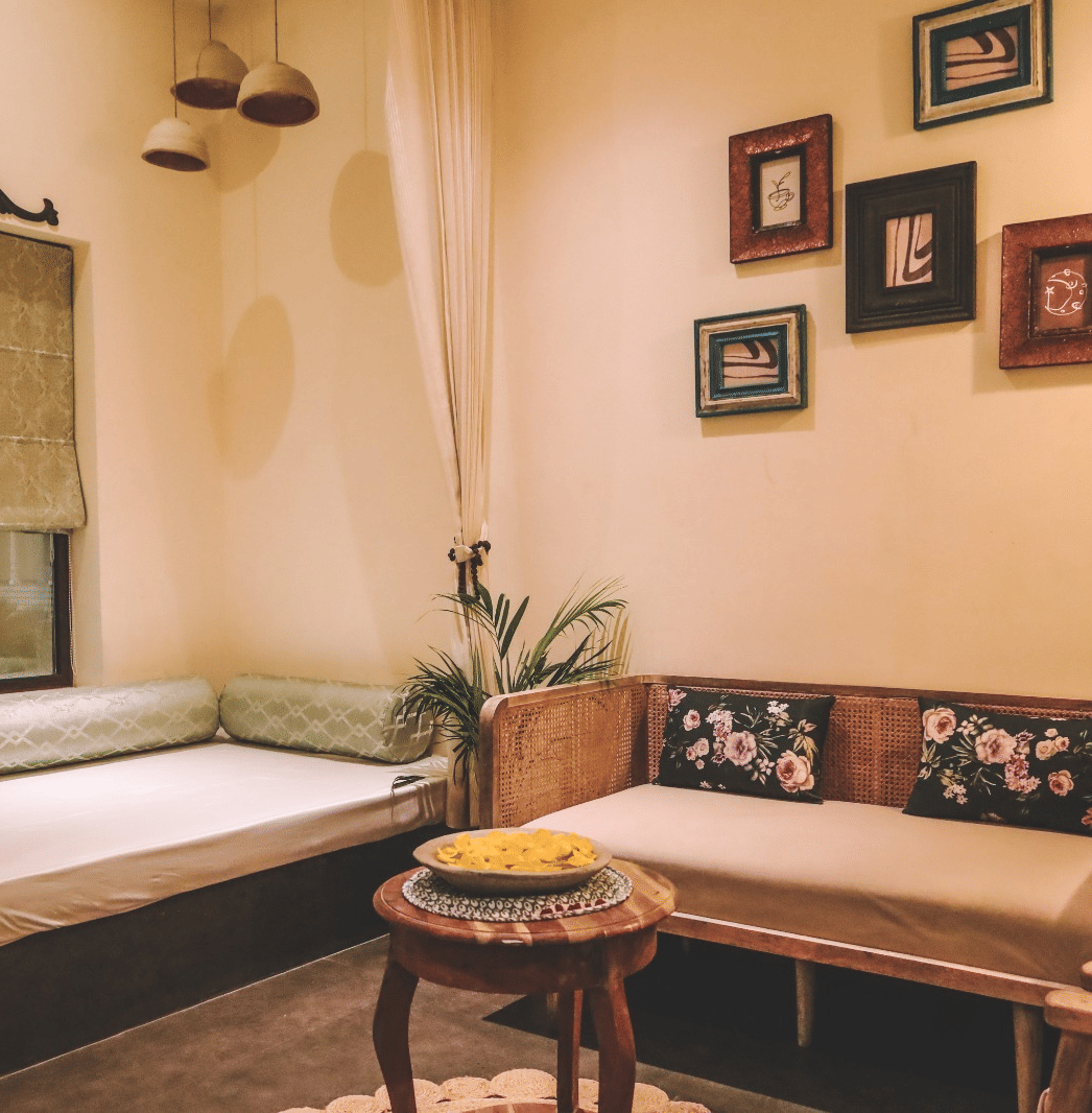 Seating area with wooden sofa, table, wall frames and window with curtain at Beelwa Palace, Jaipur