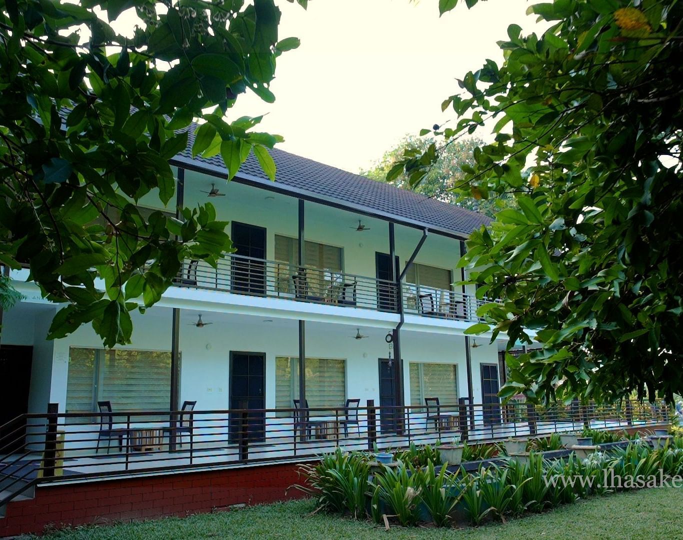 A two-story building with a porch, surrounded by a green lawn and trees.