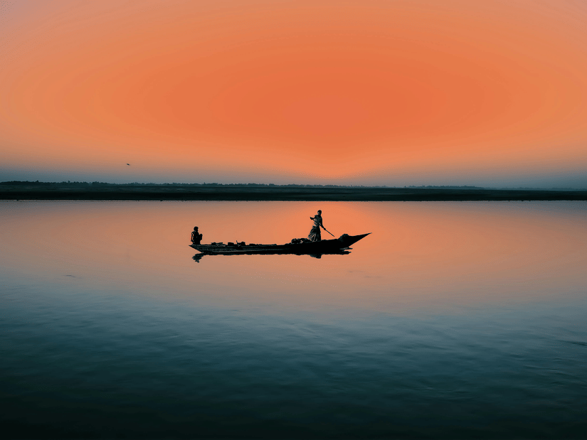 A silhouette of a fisherman in a small boat on a calm lake, set against a vibrant, deep orange sky.