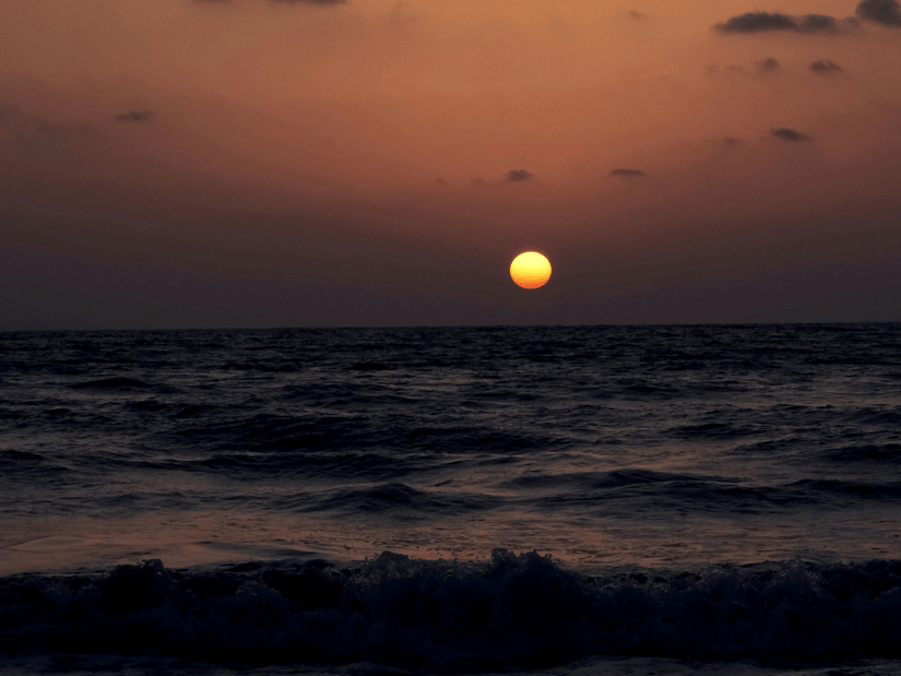 A view from the beach of the sun setting over the horizon at Aksa Beach, with different hues in the sky