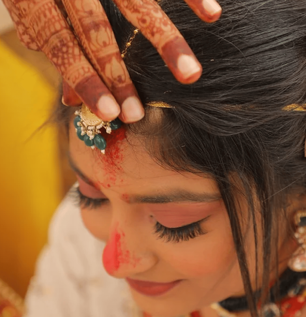 Image of a woman having her maang tikka adjusted.