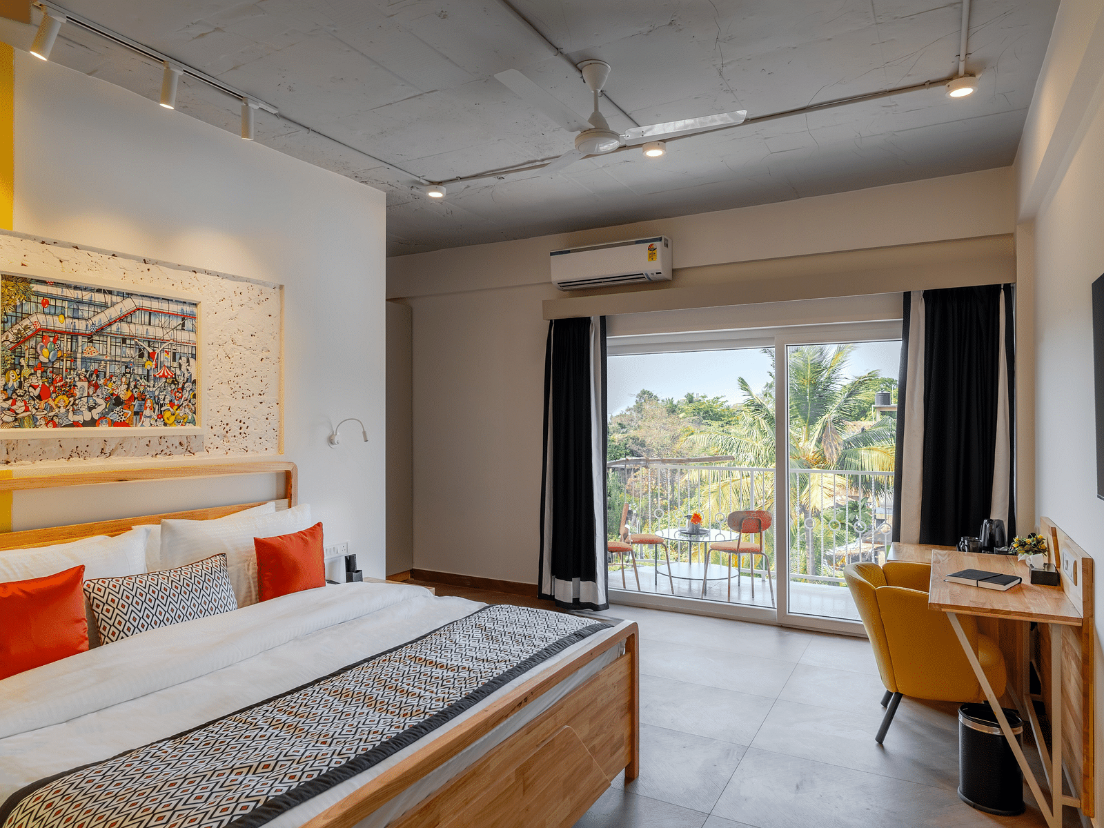 Bright hotel room with, flat TV screen, work desk and chair, vibrant art on the wall, and an access to the balcony at Bedzzz Xclusiv Morjim, Goa