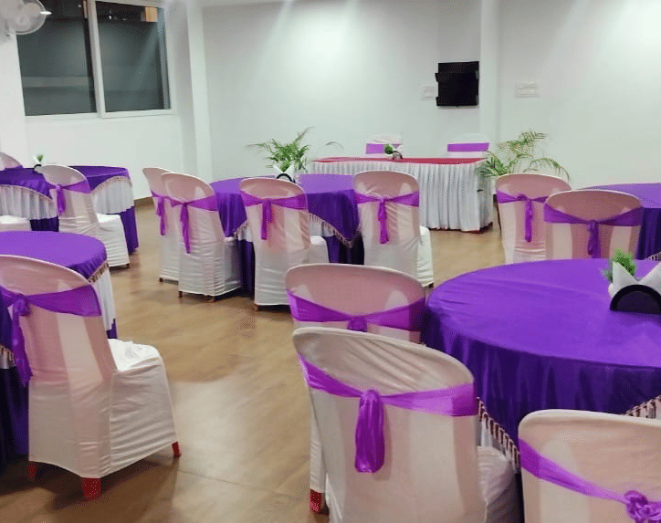A room set for an event with tables and chairs decorated with striking purple tablecloths and sashes at Coorg Orange Blossom Resort and Spa.