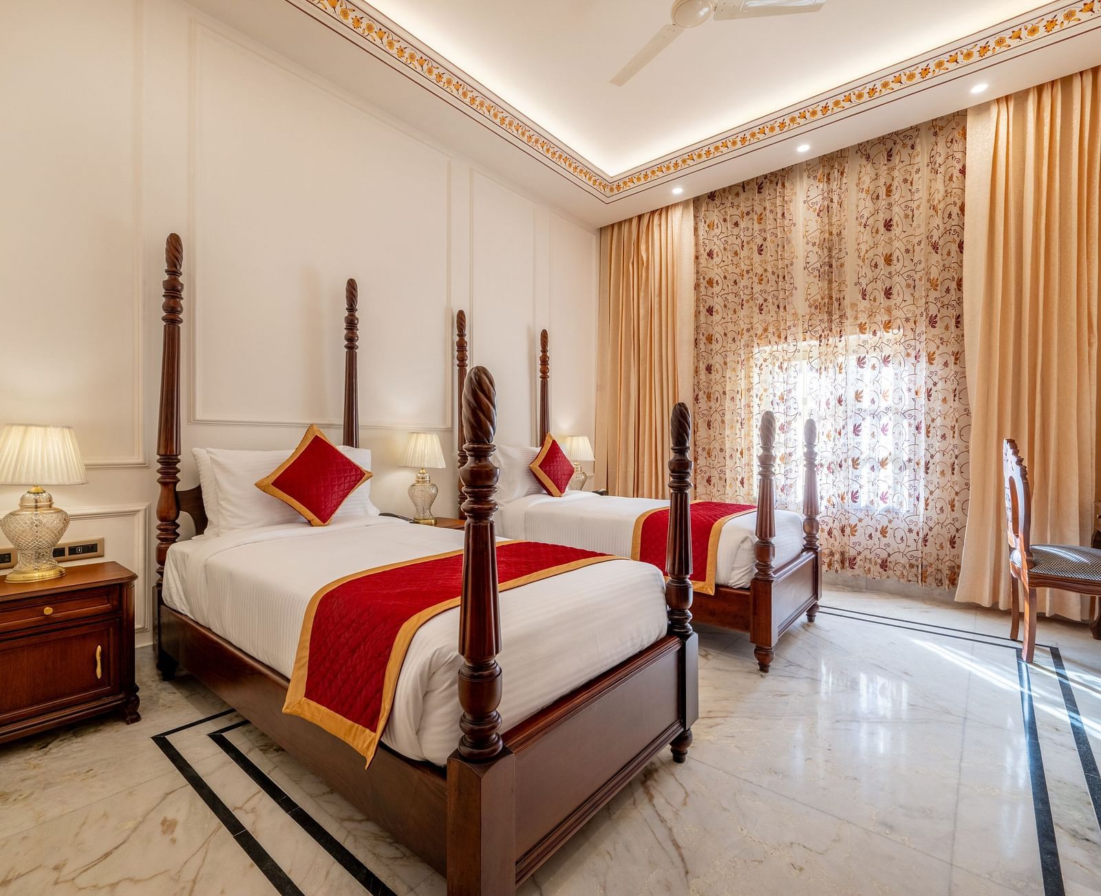 corner view image of a twin bed room along with a work desk and chair with tall golden curtains covering the window - Brij Castle, Jaipur