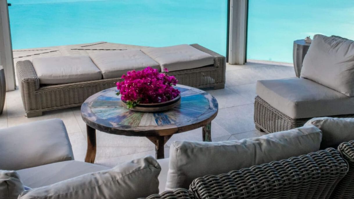  Balcony lounge area overlooking a pristine tropical beach with calm waters and distant sailboats.
