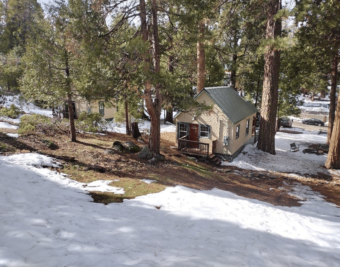 A sub-aerial view of the exterior of Shaver Lake Village Hotel surrounded by trees and fallen snow.