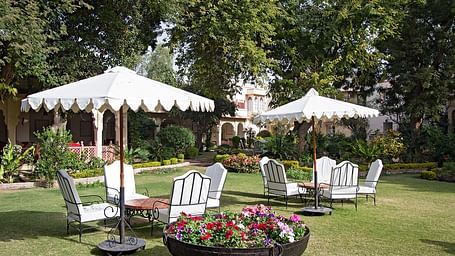 A lawn with comfortable white chairs under sunshades at Rohet Garh