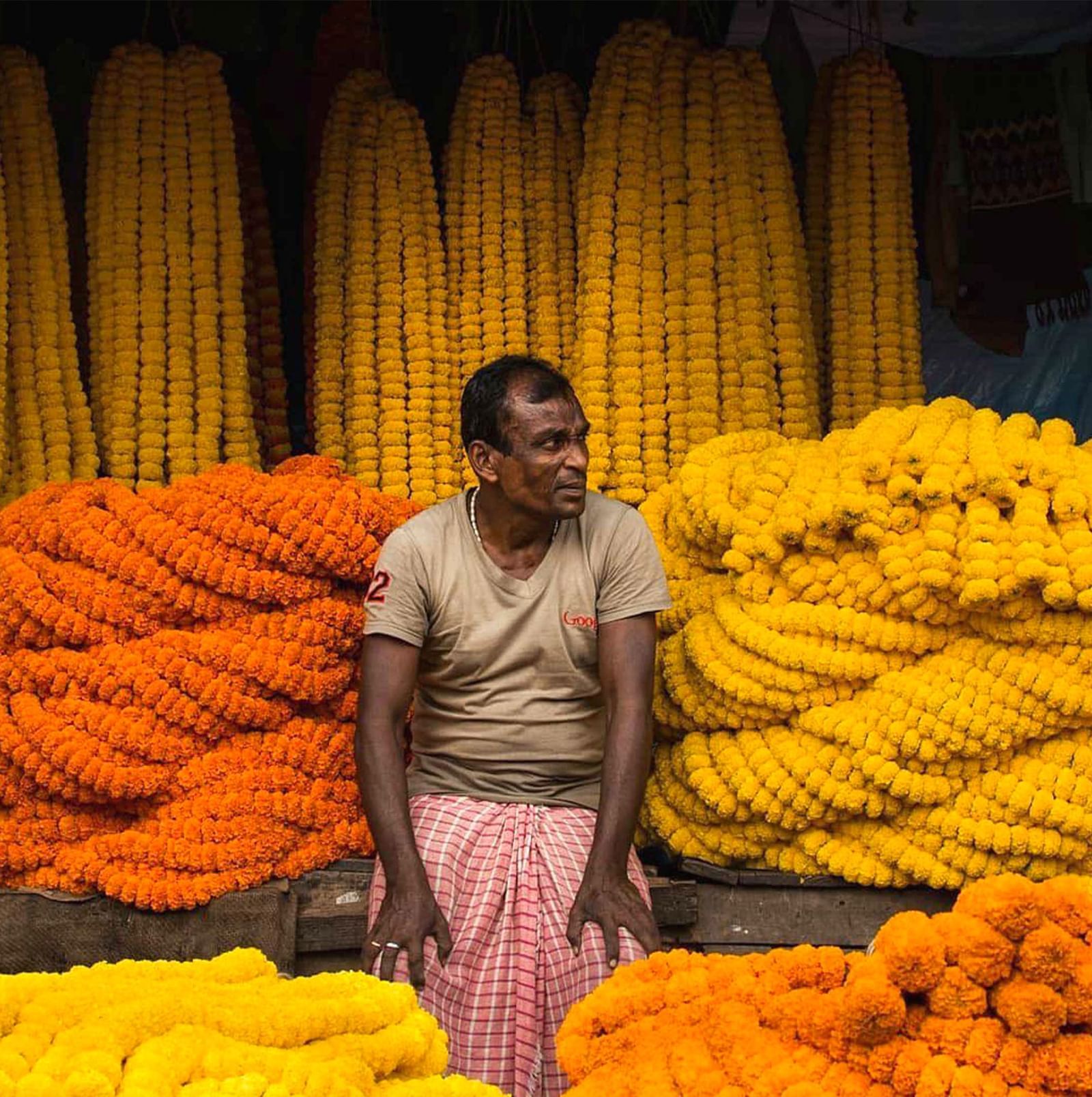 Man standing among stacks of orange and yellow marigold flowers at a market.