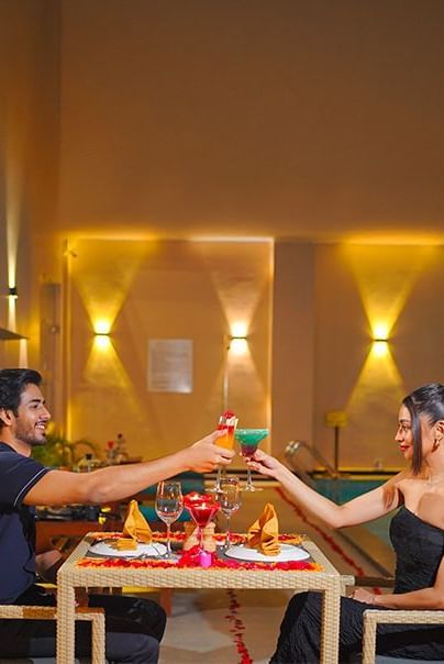 A couple clinking their cocktails by the pool at a restaurant in Agartala - Polo Hotel Agartala