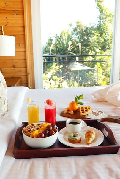 Breakfast tray with juice, fruits, and dishes placed on bed at Polo Resort Cherrapunjee.