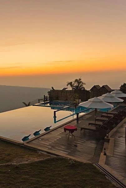 Sunset view of infinity pool with lounge chairs at Polo Resort Cherrapunjee.