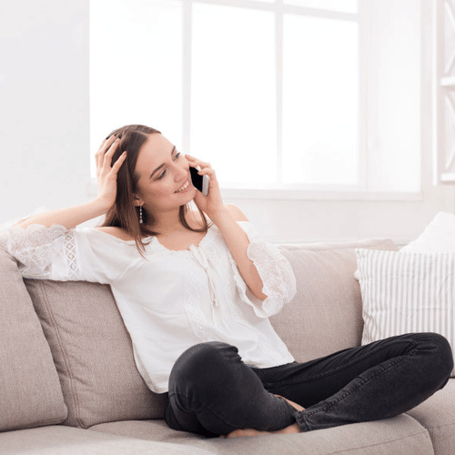 A woman smiling during a phone call on sofa with her one hand on her head at YO1 Longevity & Health Resorts
