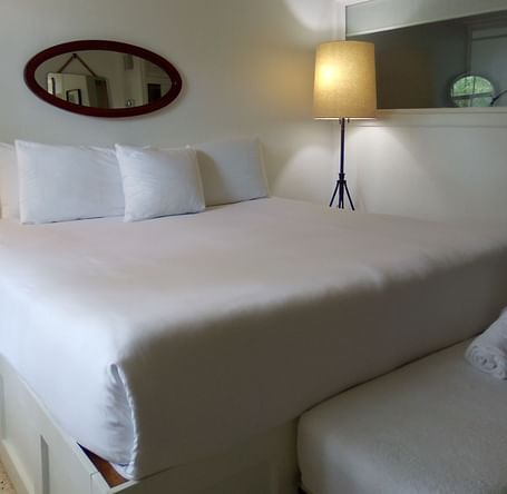 A single bed at Casa Morada with white bedding, a floor lamp, and an oval mirror mounted on the wall above the headboard.