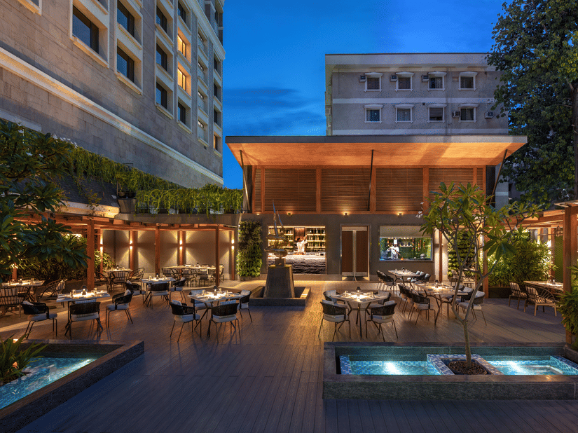 An outdoor dining area with tables, chairs, and plants, illuminated by warm lighting along with swimming pool. 