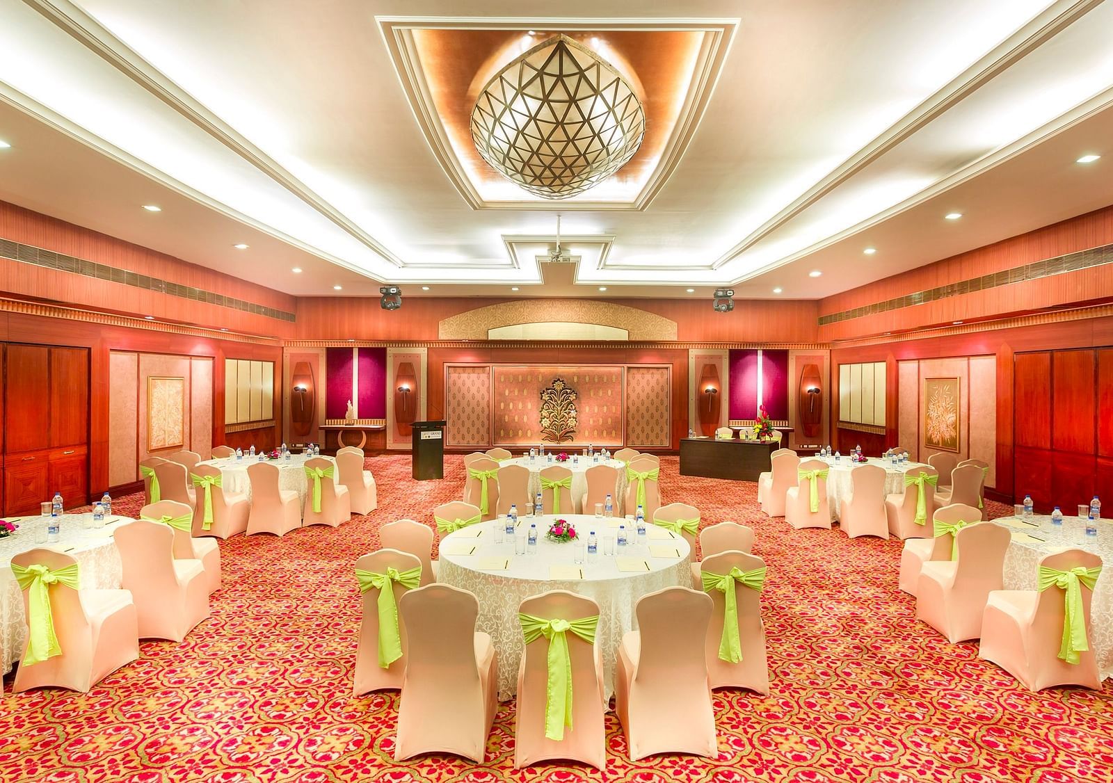 A wedding hall with white chairs tied with yellow ribbons pointing towards the stage at Grand Chennai By GRT Hotels.