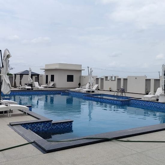 Rooftop swimming pool with tiled edges, surrounded by lounge chairs and closed umbrellas; cabanas in the background and a hose lying across the pool deck in the foreground under a partly cloudy sky - Kyriad Prestige, Ilkal