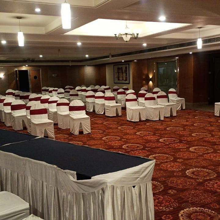 Large banquet hall of Lords Plaza Ankleshwar featuring neatly arranged chairs, a carpeted floor, and modern interiors