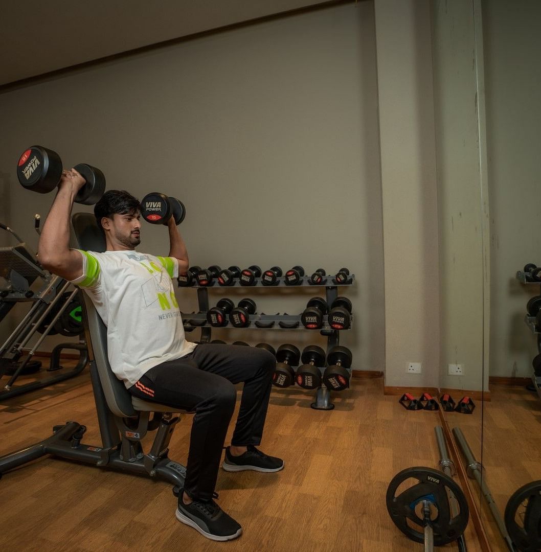 A person performing the shoulder press with dumbbells at the indoor gym at Singalila Club
