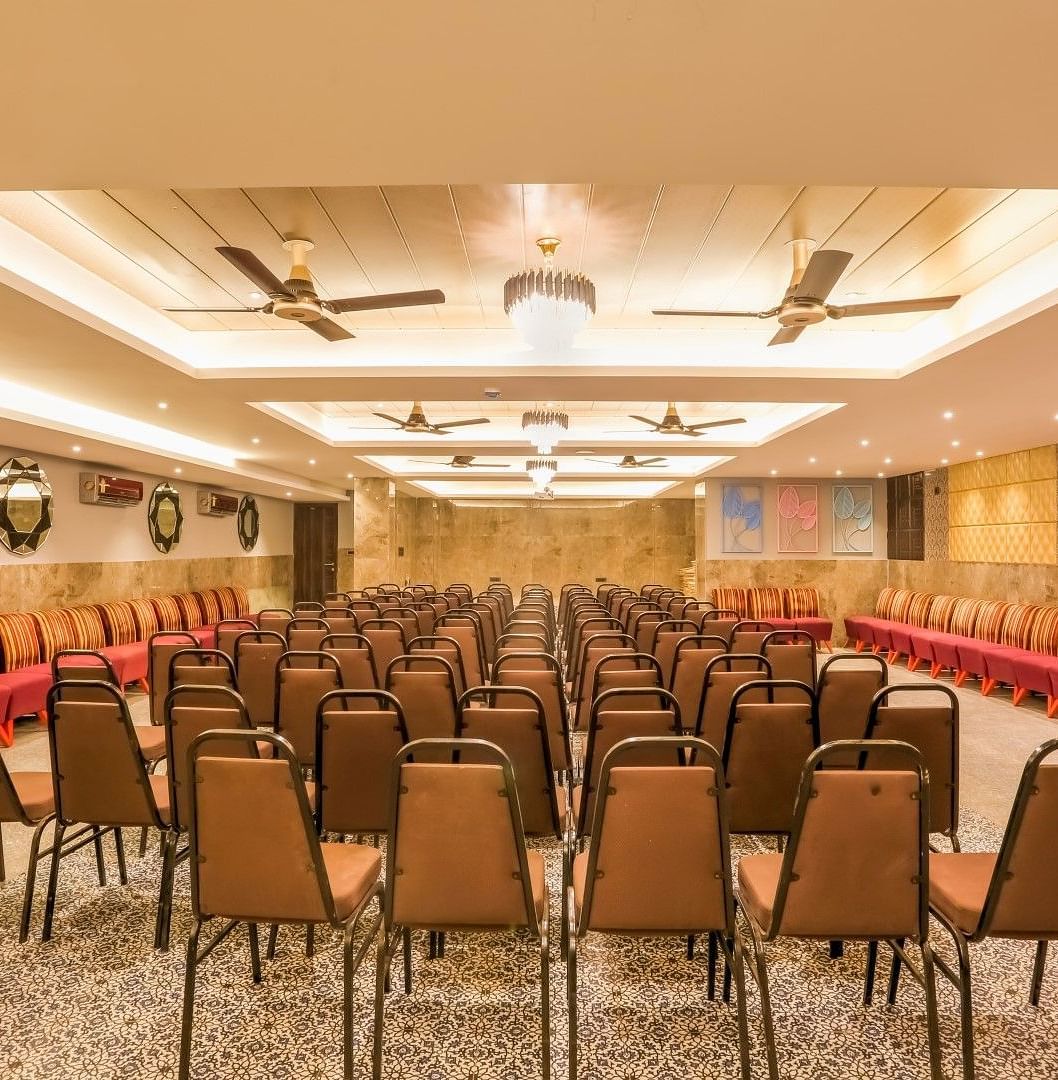 Rear view of the banquet hall, highlighting chairs meticulously arranged in rows, illuminated by warm lighting and accentuated by overhead ceiling lights