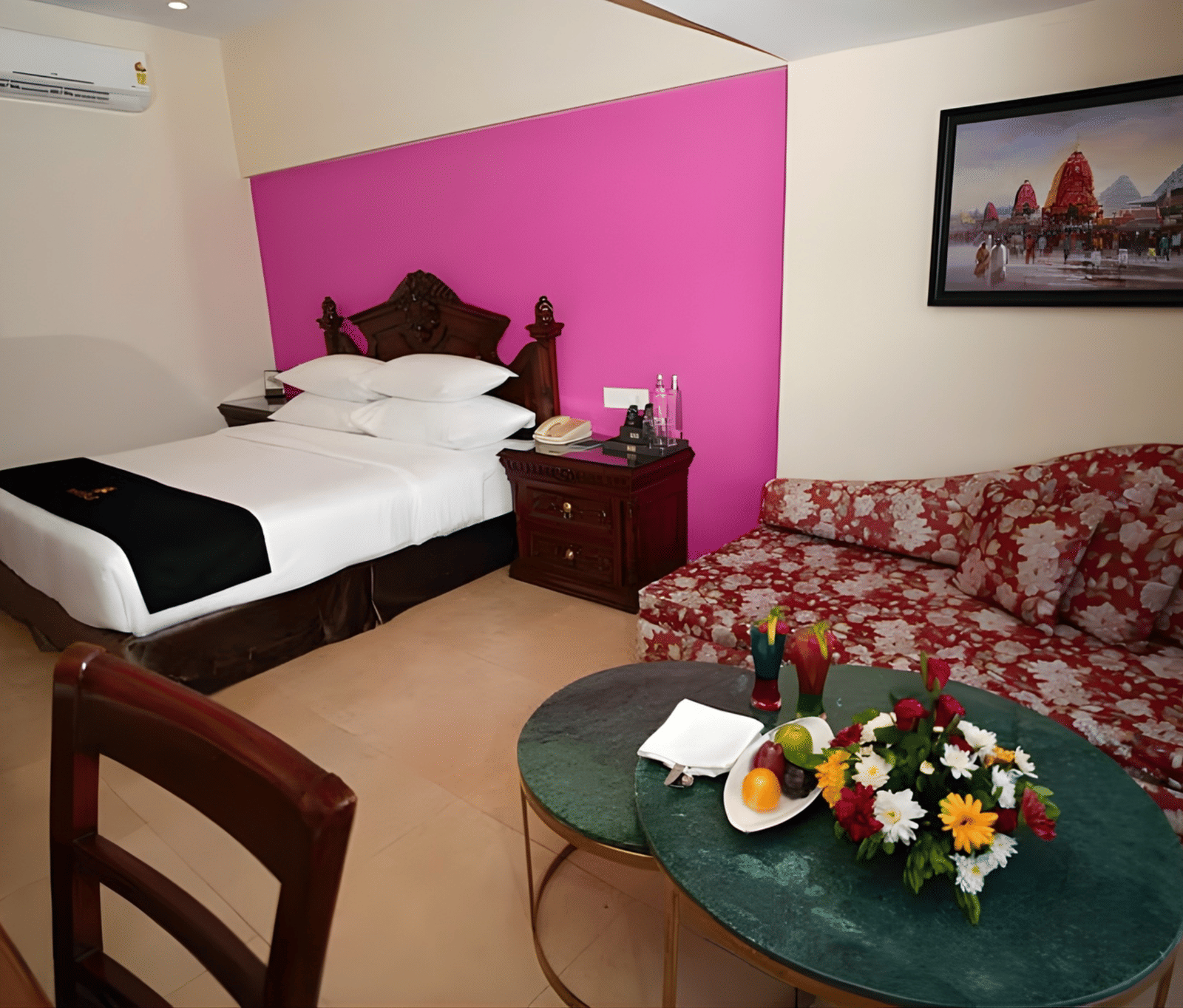 Modern MAYFAIR Heritage Puri hotel room with elegant black and white bedding, vibrant pink accent wall, and cozy green velvet seating area with fresh fruit platter.