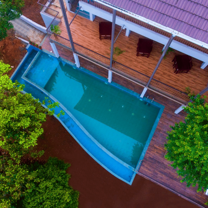 An aerial view of a swimming pool with an edge blending into the forested background, reflecting the trees and sky at Abad Brookside Lakkidi, Wayanad, one of the premier luxury resorts in Wayanad.