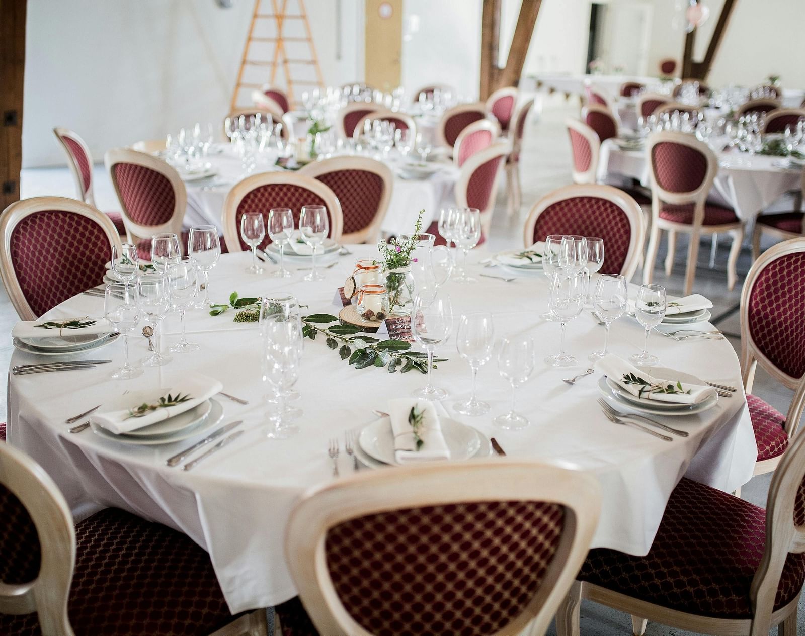 Tables set for a formal event with elegant white tablecloths and red chairs.
