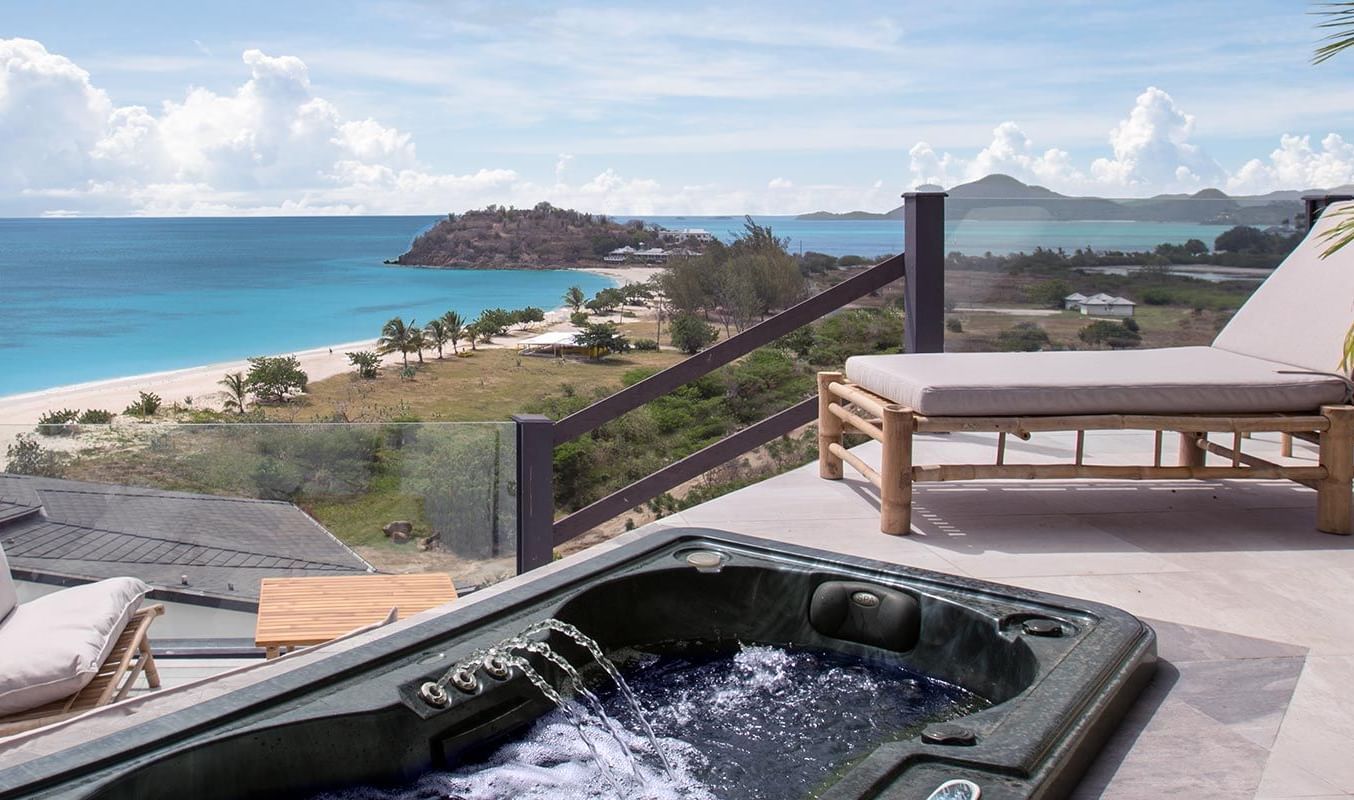 Luxury ocean-view terrace with lounge chairs and a hot tub overlooking a beach and coastal cliffs.
