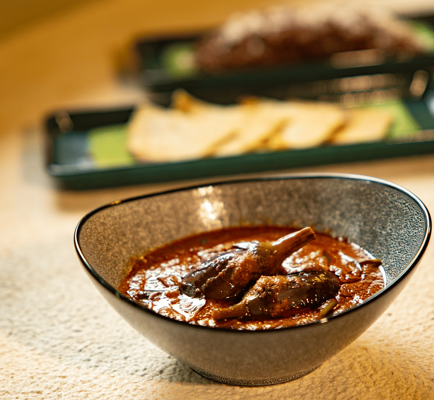 A bowl of rich, dark meat curry at Stanley Revelation, with other dishes blurred in the background.