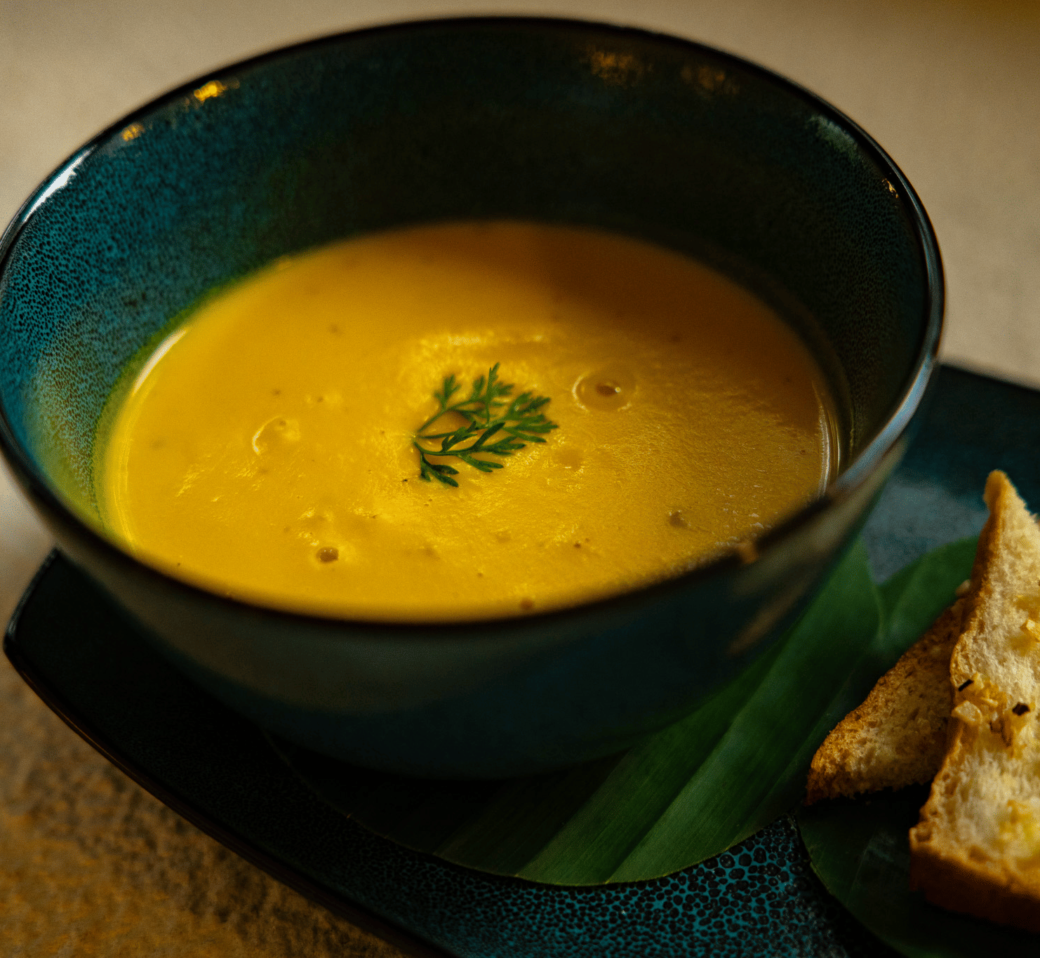A bowl of golden-coloured soup with a garnish of herbs at Stanley Revelation, served with toasted bread.