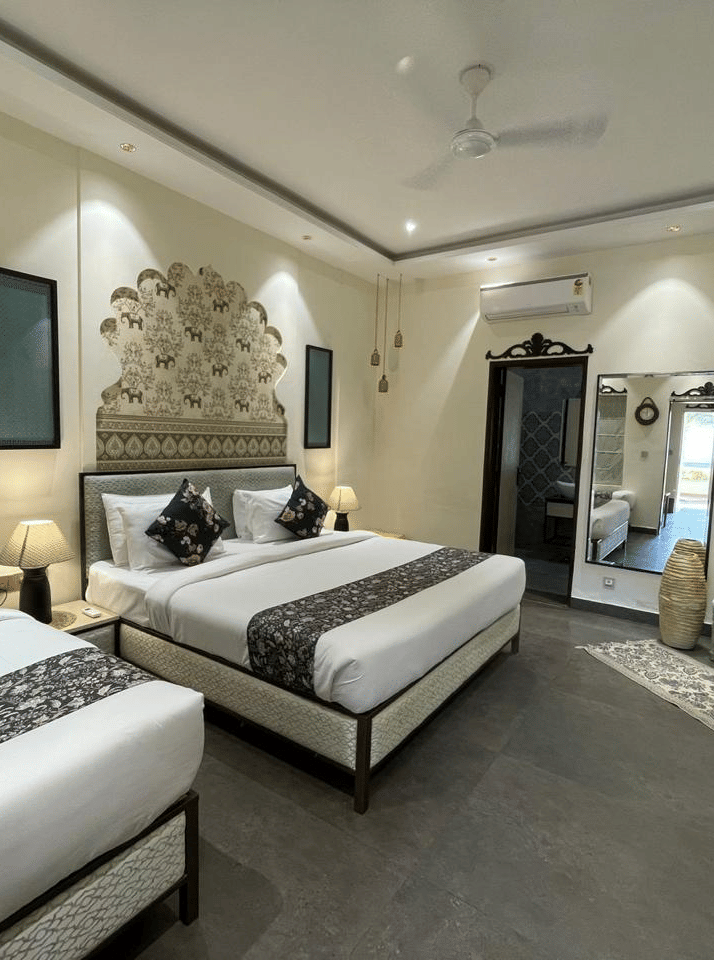 2 single beds with wall decor and lamps beside a mirror and armchair at Beelwa Palace, Jaipur
