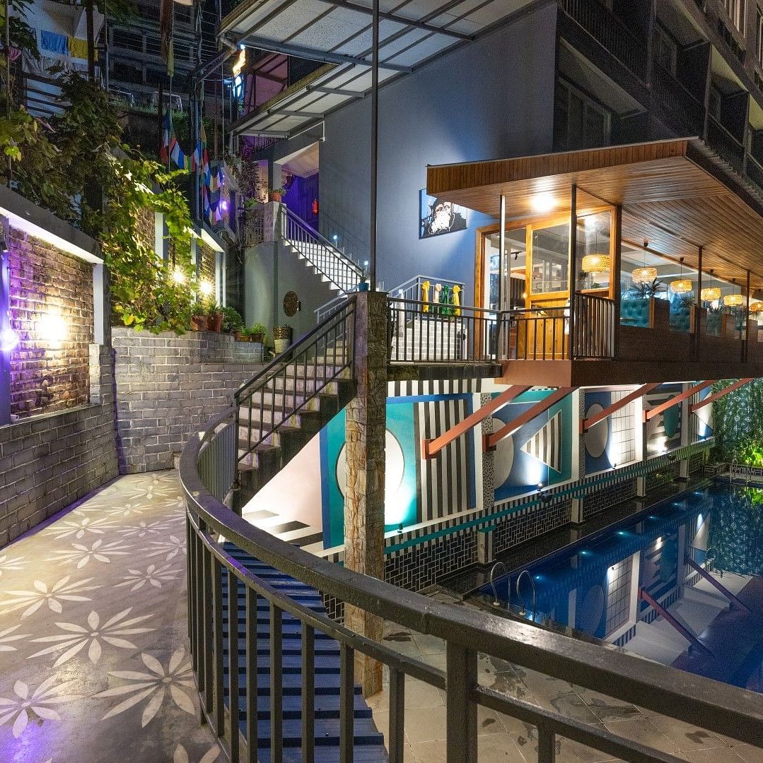 An image of a entrance which has a swimming pool on one side and the entrance leads to a well lit building - Avianna Group of Hotels & Resorts