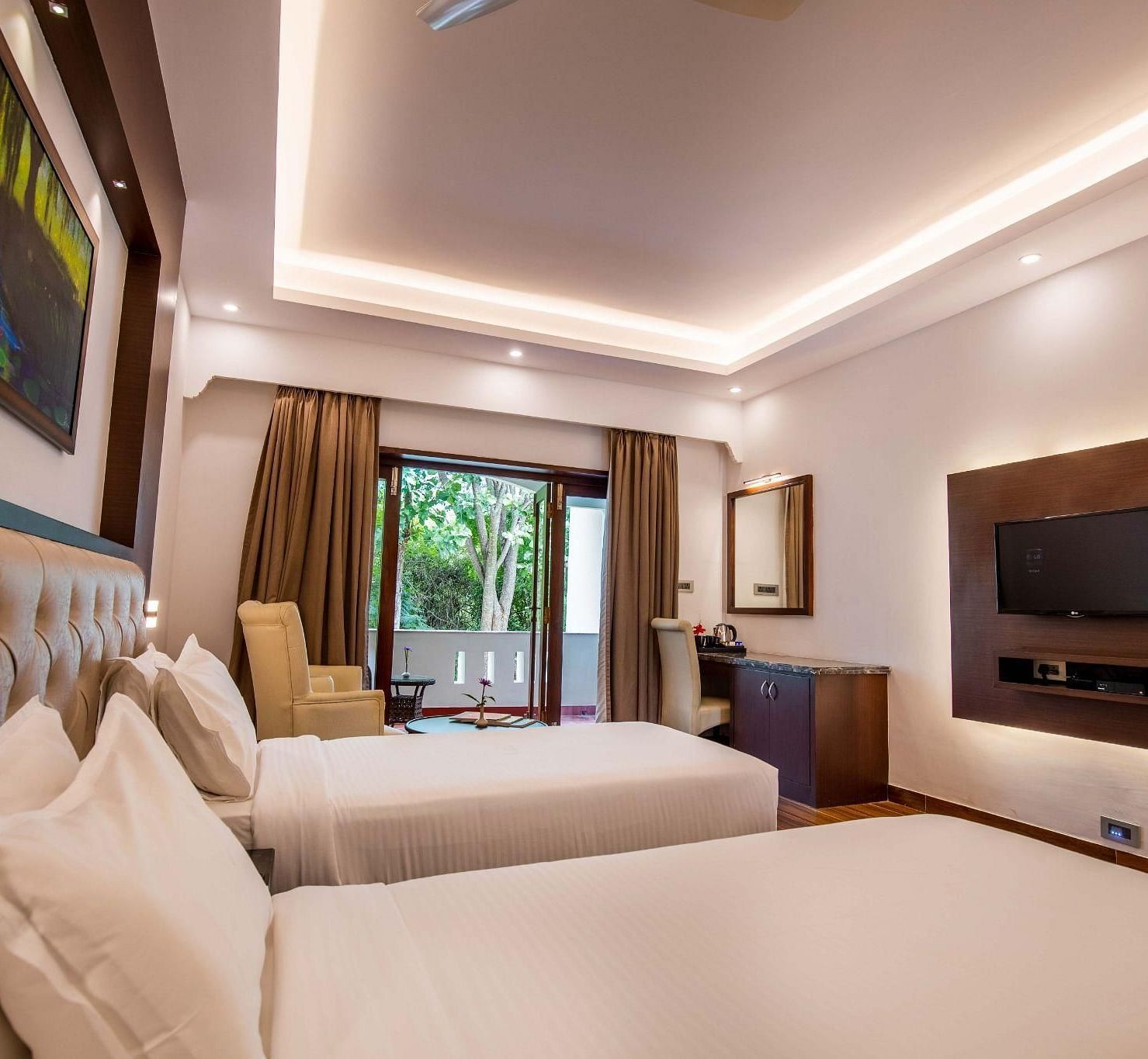 A room filled with two single cot, a tv, table and big glass windows at Avana Resort