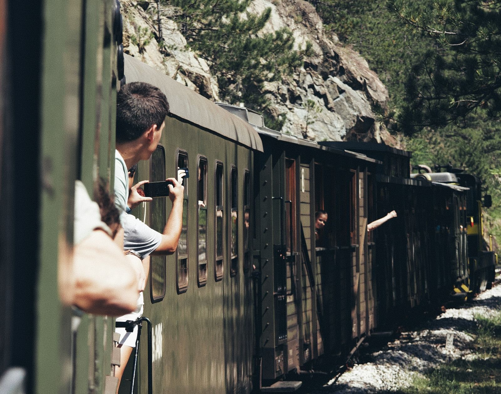 An overview of a train that is travelling on a forest area with people looking out.