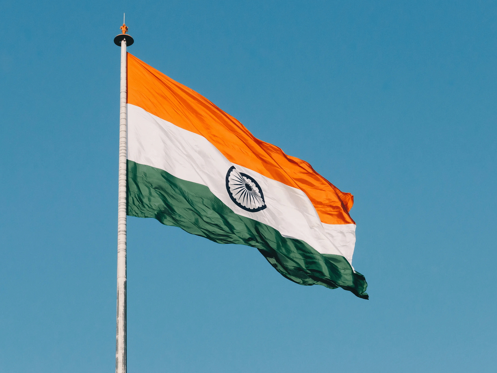 The Indian national flag, with its saffron, white, and green bands and the Ashoka Chakra in the center, waving against a clear sky.