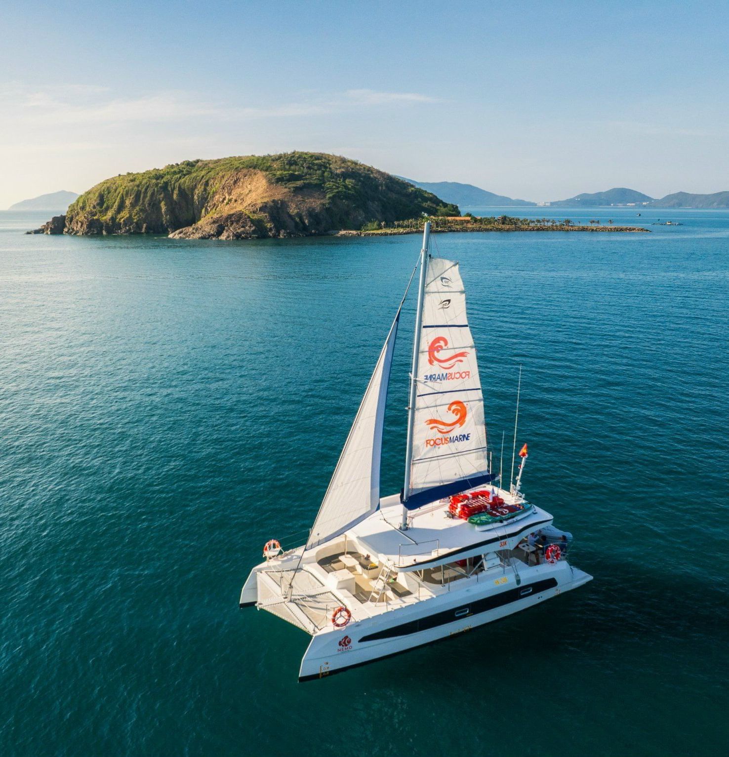A sleek catamaran sailing on turquoise waters with island views, offering scenic marine adventures from Alibu Resort.