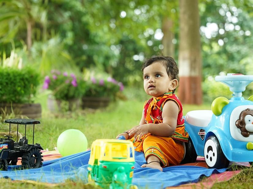 A baby sits on a blanket surrounded by colourful toys