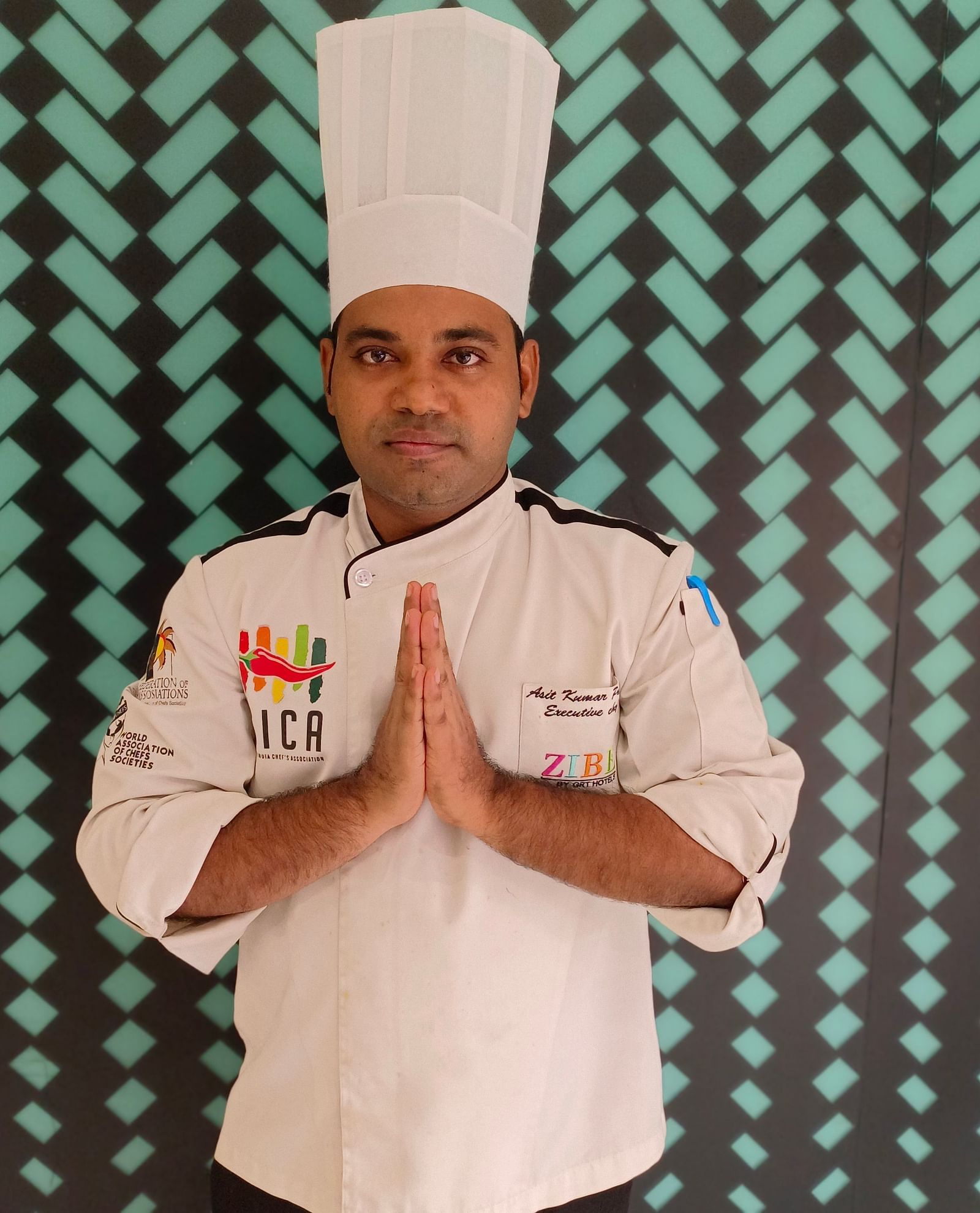 MR. Asit Patra stands with poise against a backdrop featuring a repeating pattern.