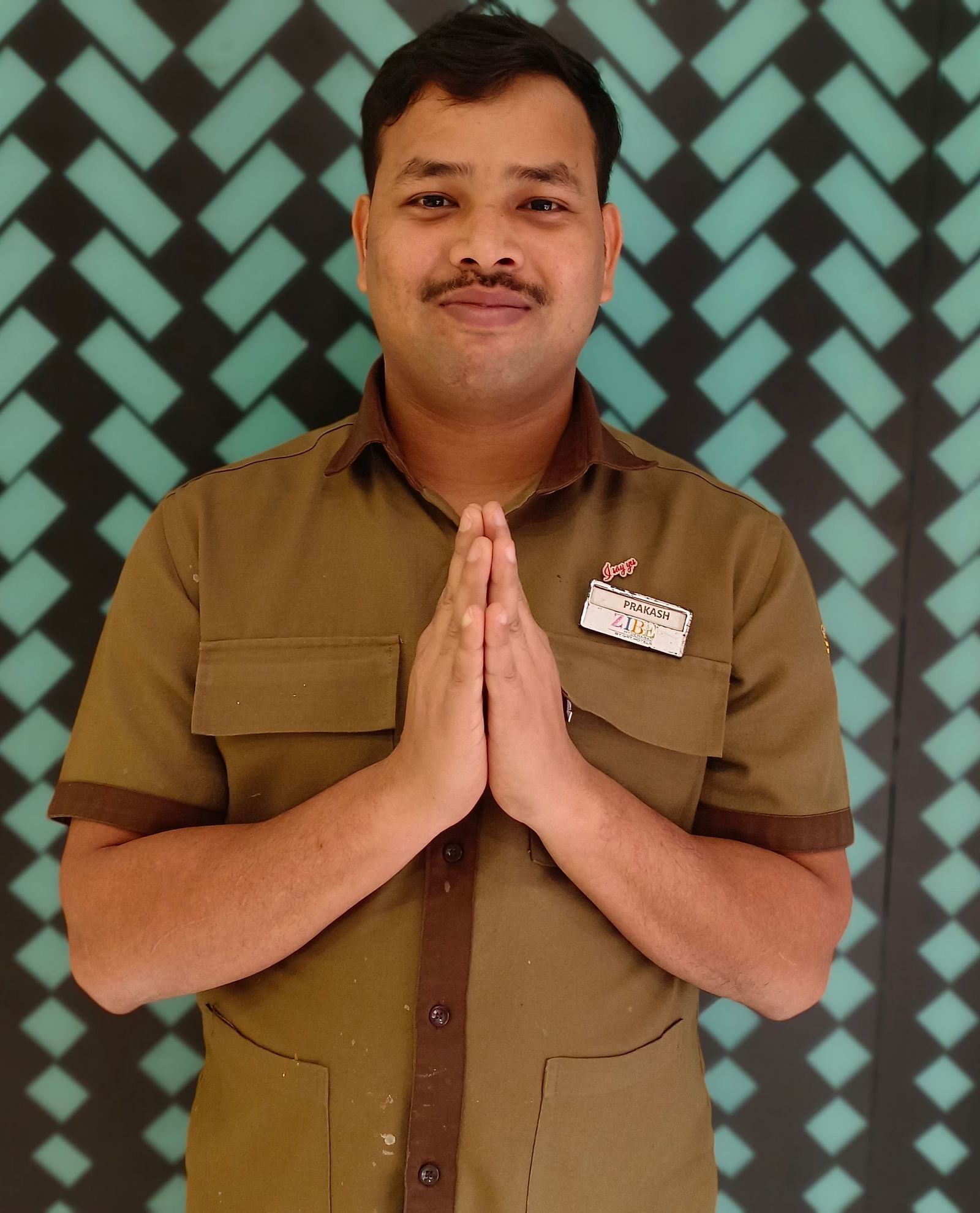 Mr. Prakash stands with poise against a backdrop featuring a repeating pattern.