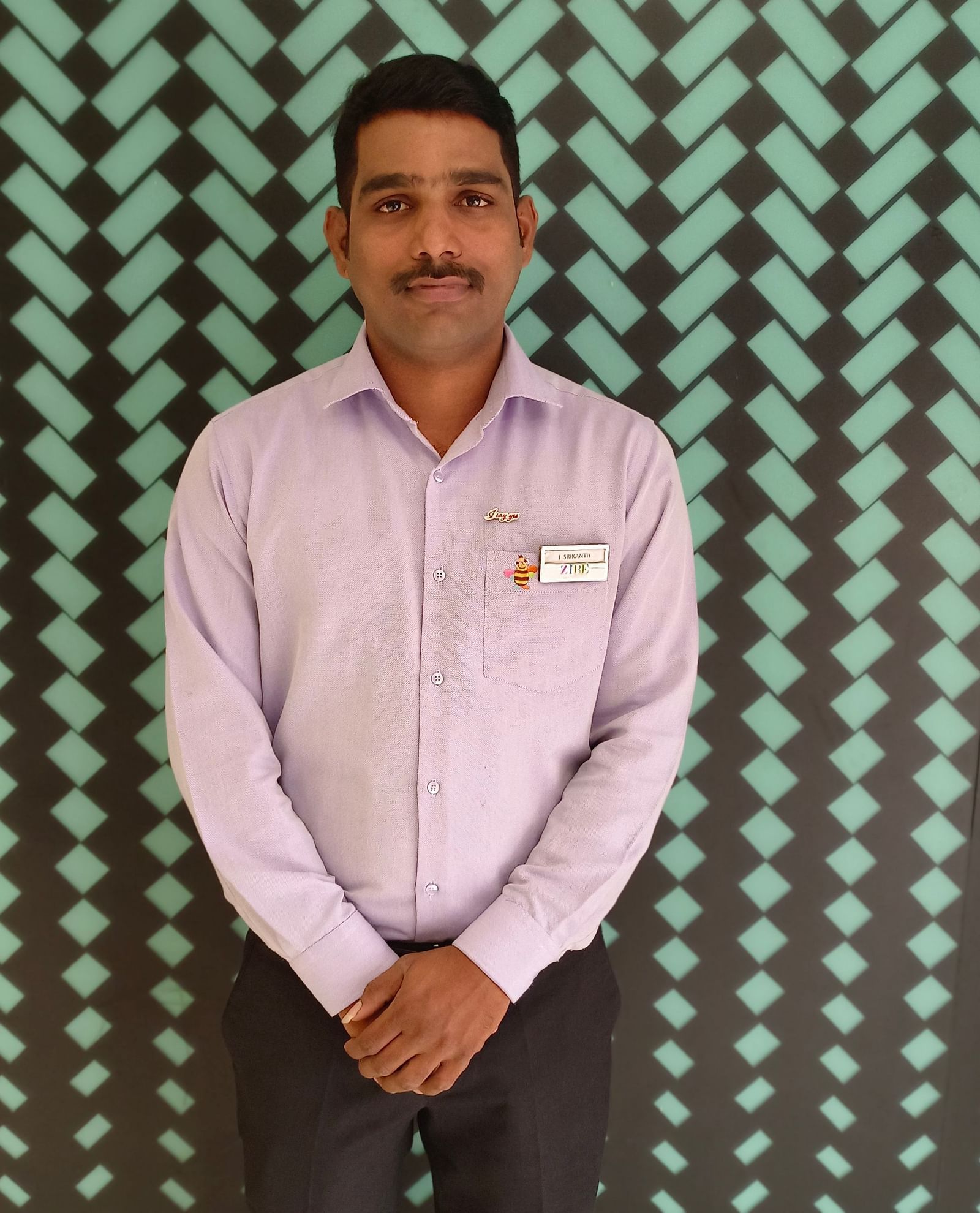 Mr. Srikanth stands with poise against a backdrop featuring a repeating pattern.