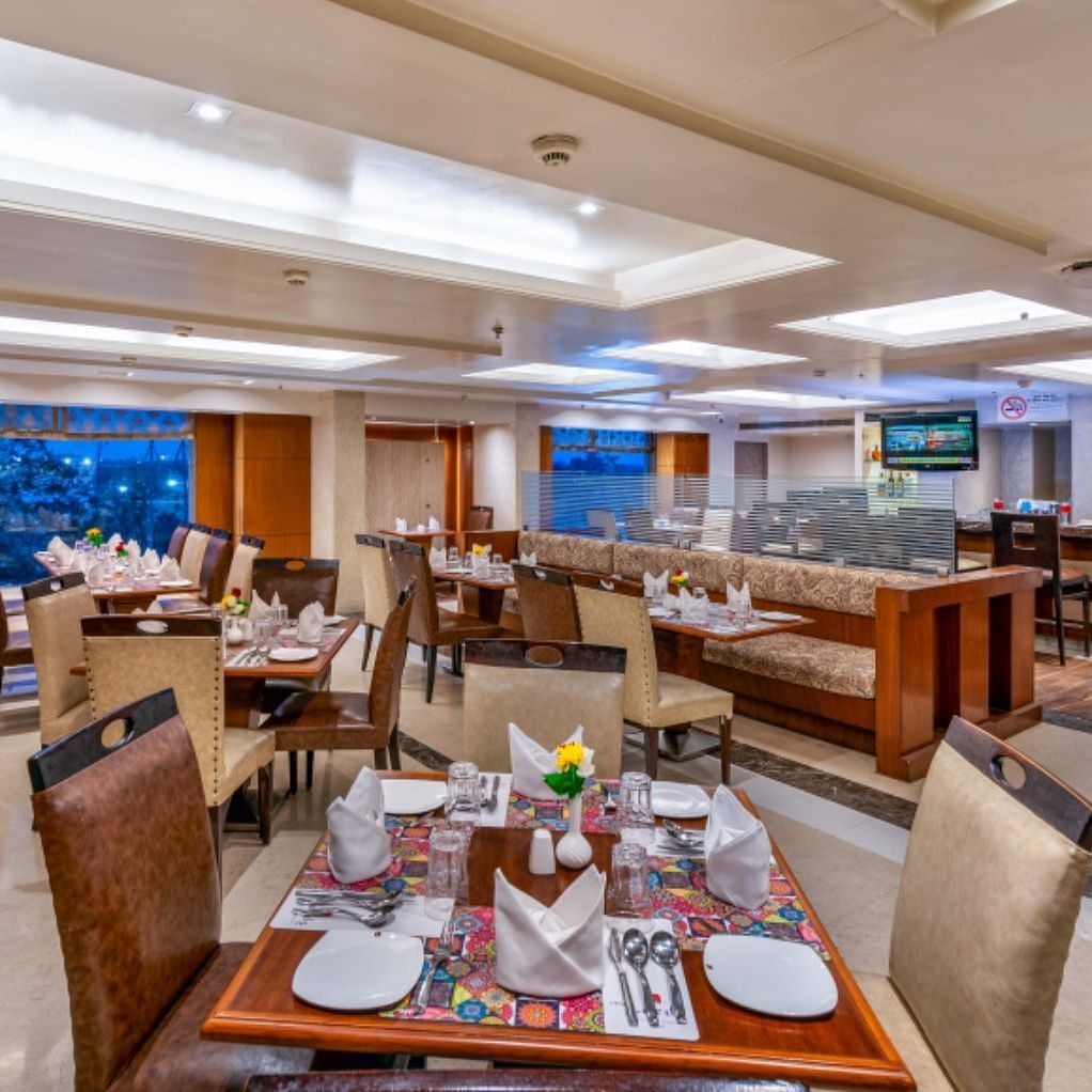 Blue Coriander Restaurant with four and six seaters and a bar counter with a wall mounted TV at Libra Lords Inn Jaipur