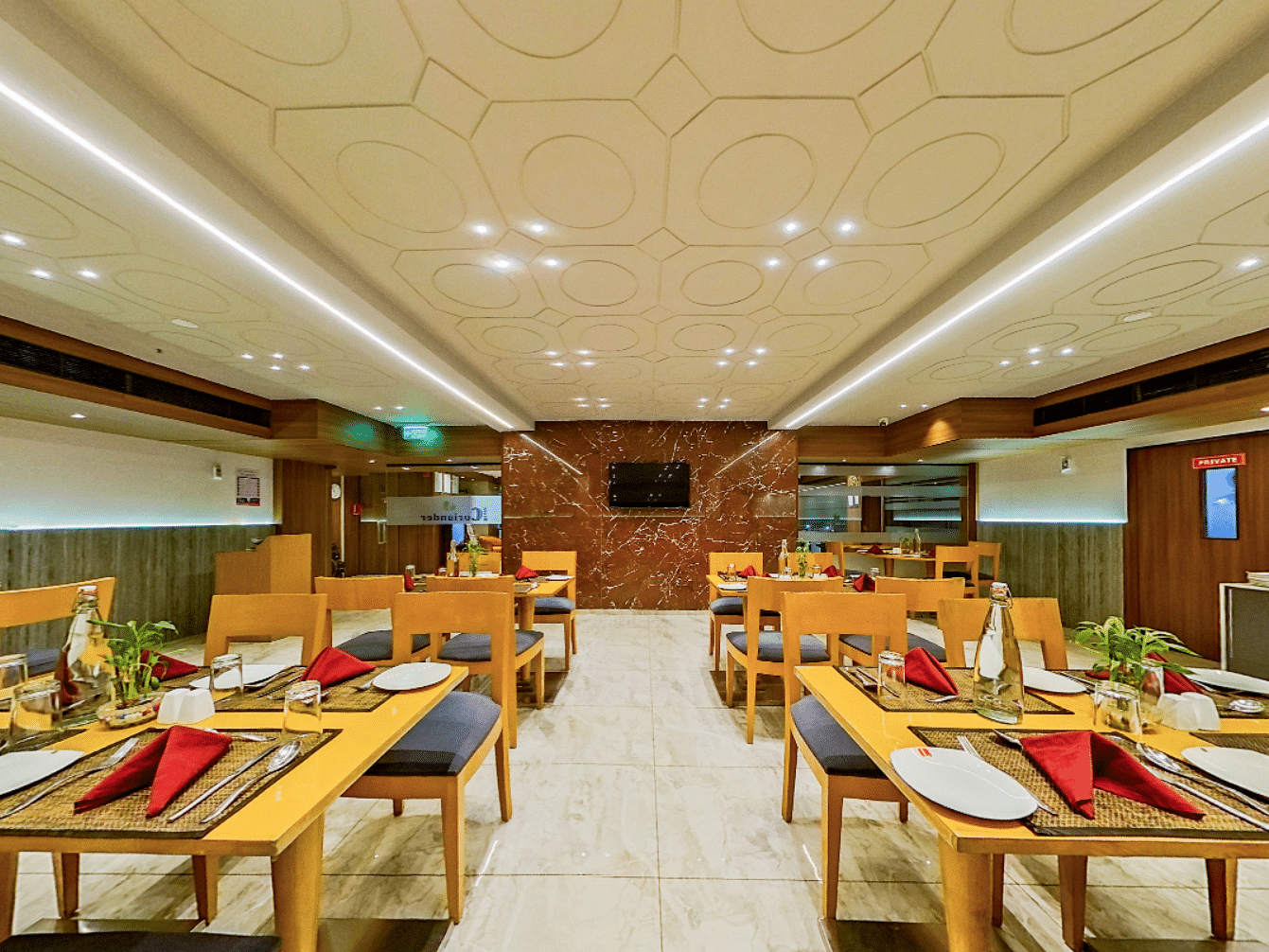Contemporary restaurant with wooden dining tables, black chairs and red napkins at Lords Eco Inn Dahej, set for guest dining service