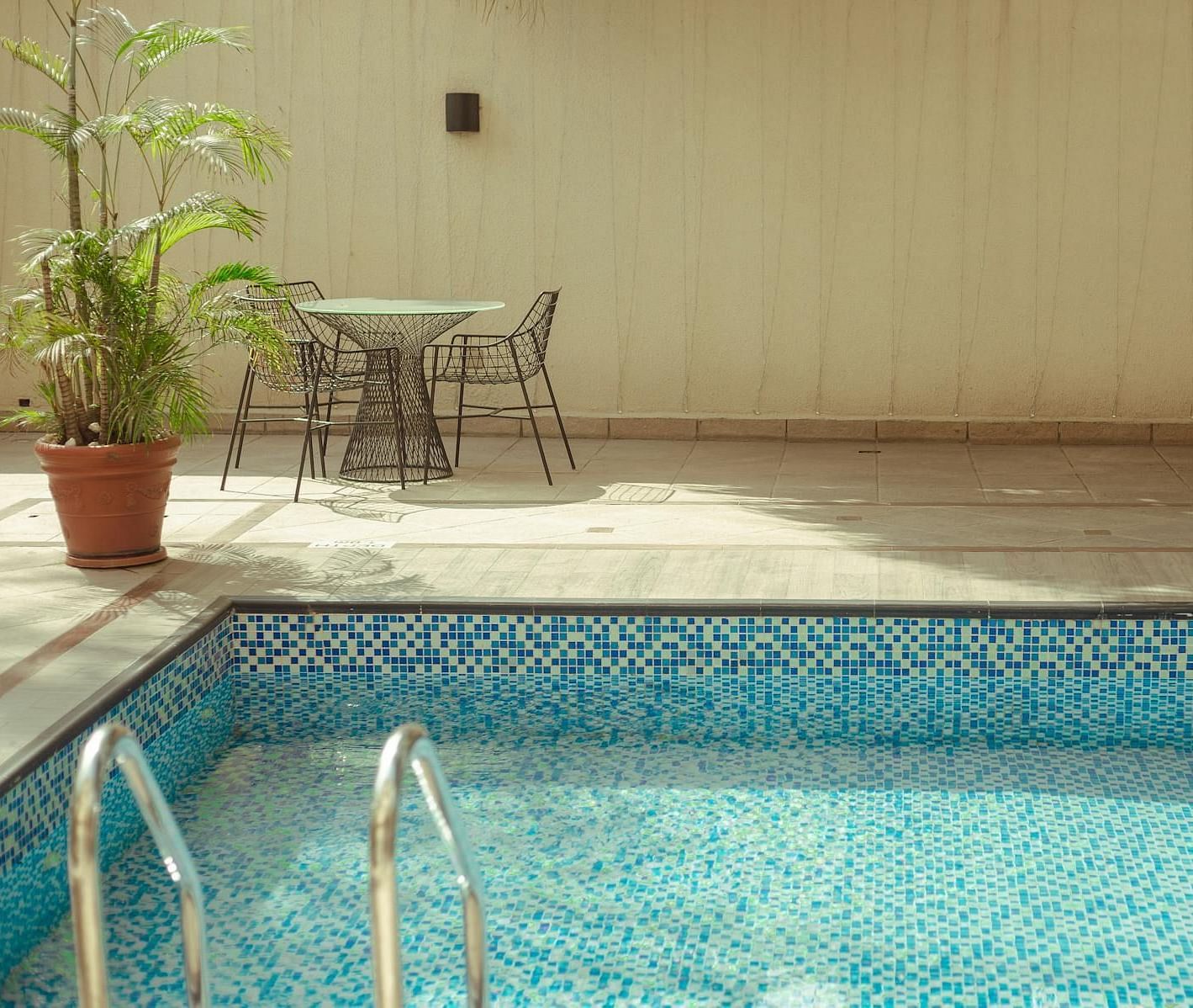 A swimming pool with a lounge chair, a small table with two chairs, and a potted plant placed nearby.